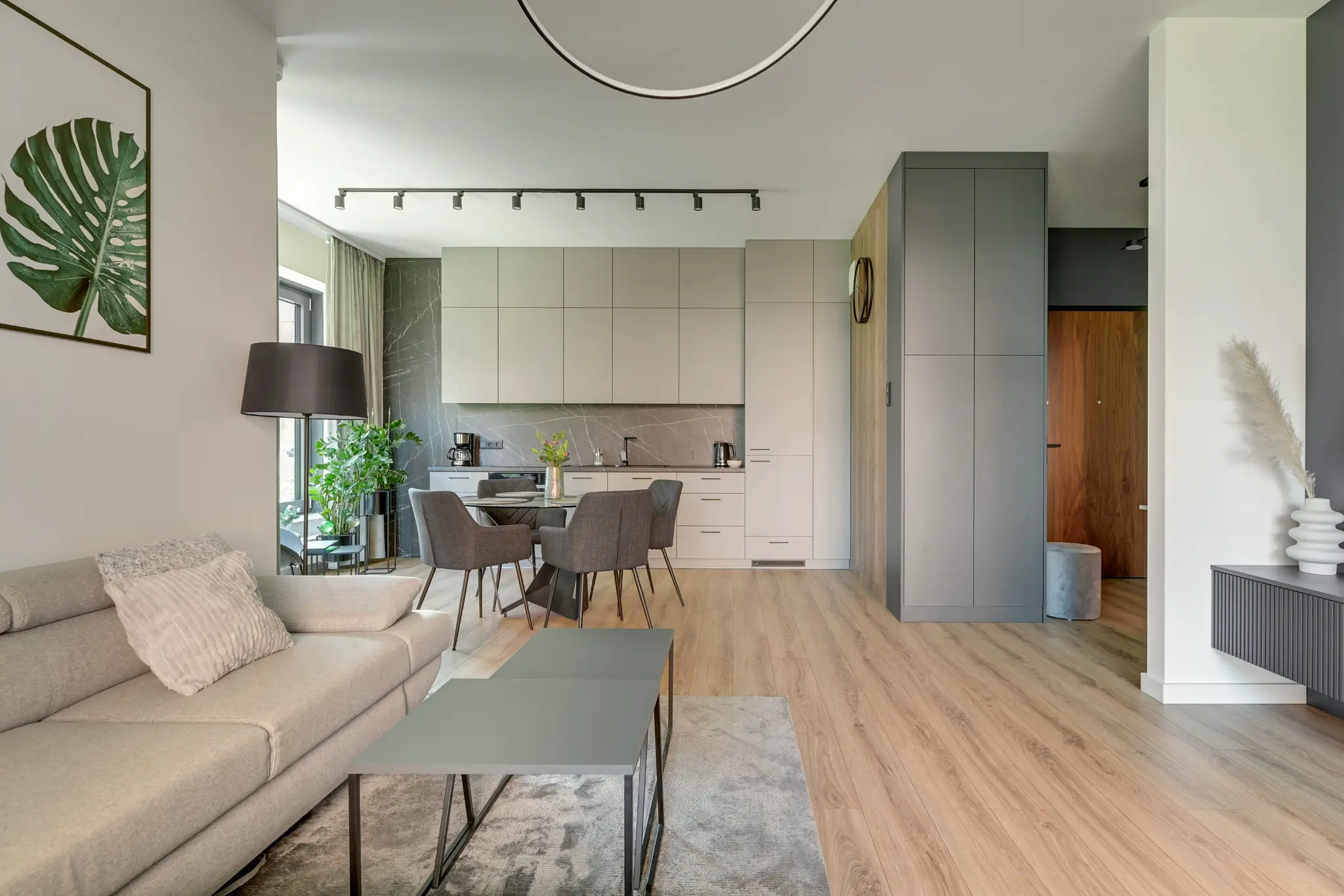 Salon apartamentu Brabank z jasną sofą, stołem, kuchnią i szarą zabudową