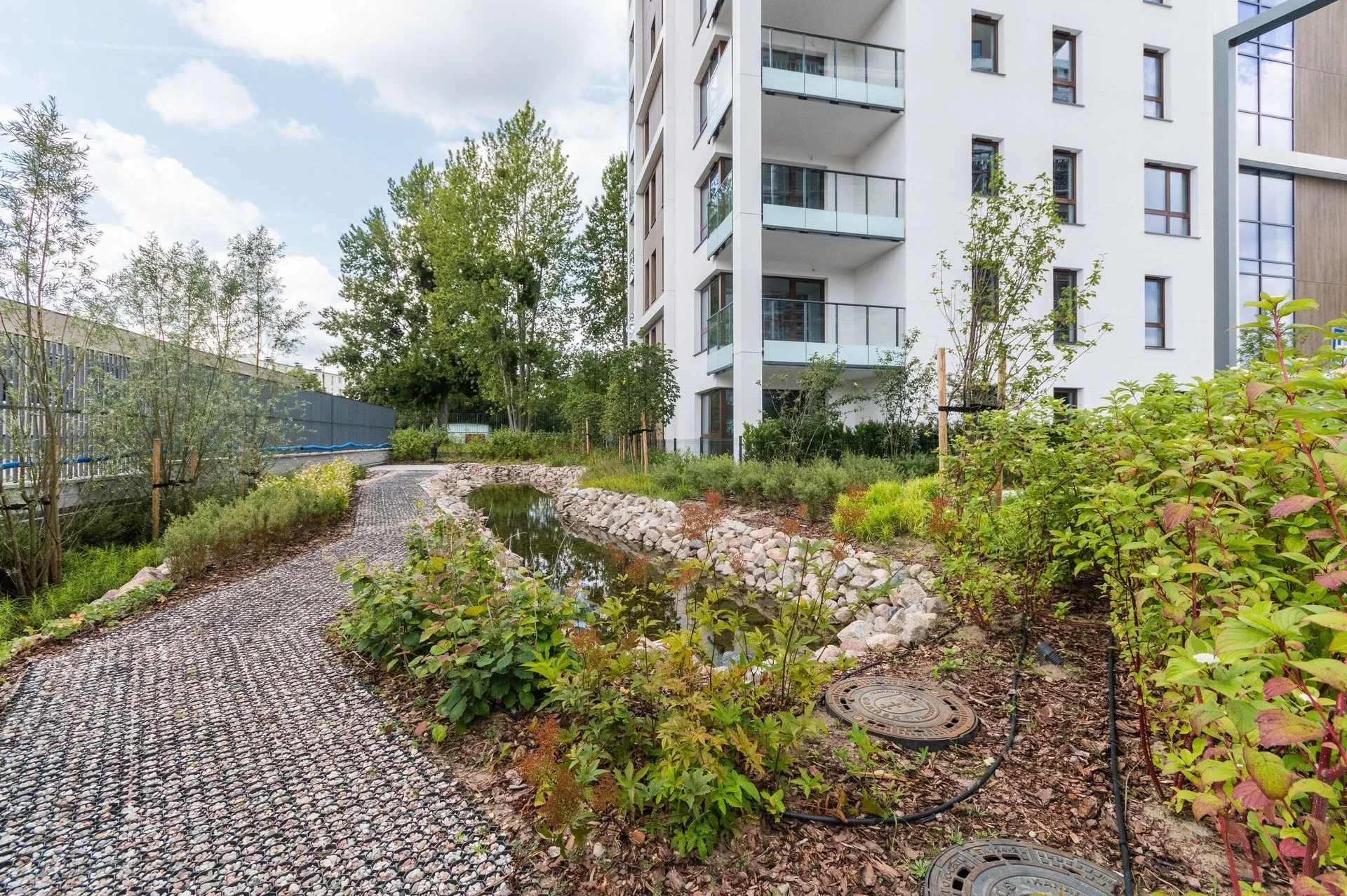 Landscaped greenery at Bulvar Apartments — path, plants and water feature next to the building