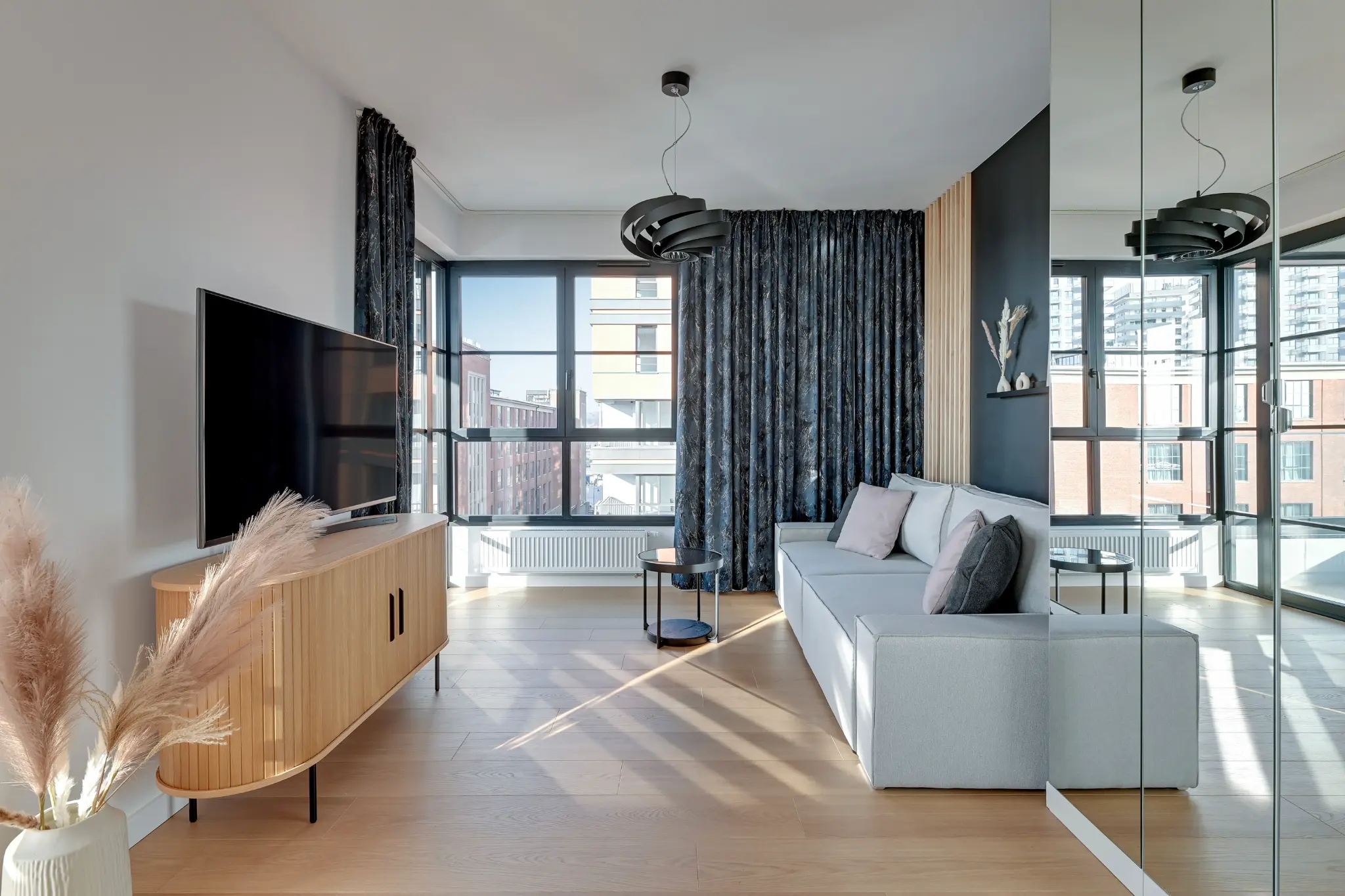 Salon apartamentu w DOKI z jasną sofą, telewizorem i lustrami