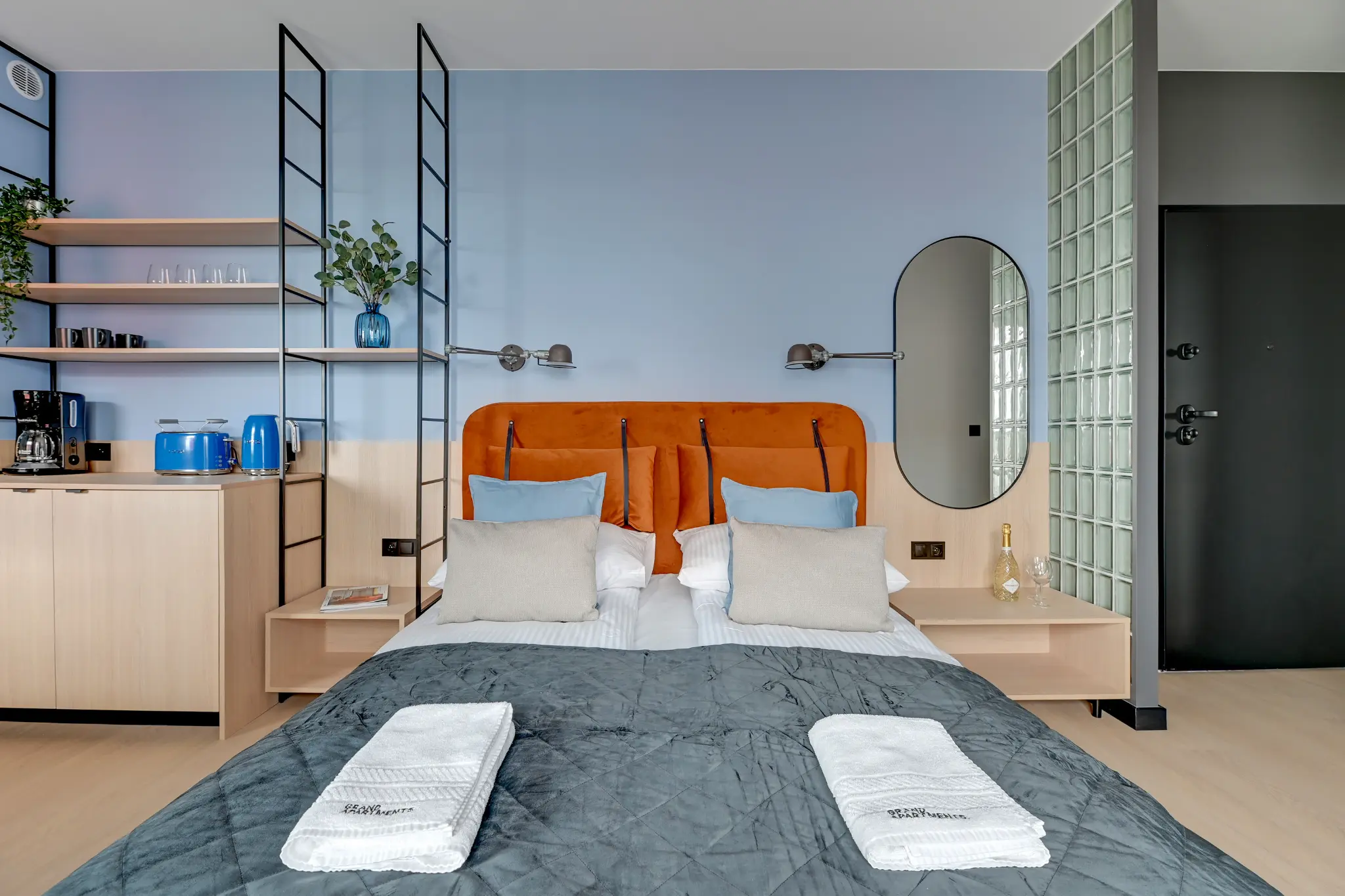 Strefa sypialna w apartamencie DOKI z pomarańczowym zagłówkiem i kącikiem kawowym