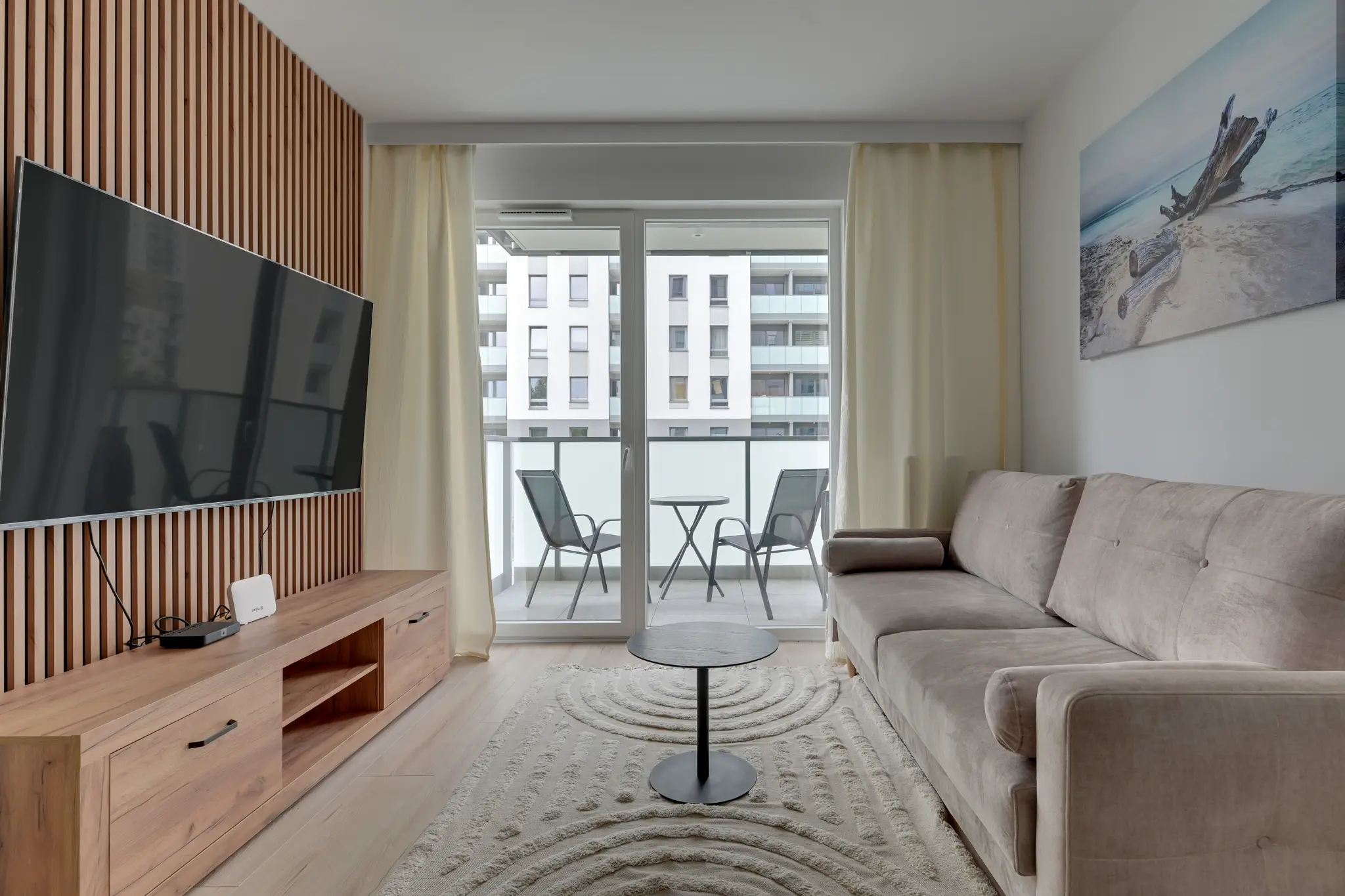 Apartament w Horizonie — beżowa sofa, telewizor na lamelowej ścianie i wyjście na balkon