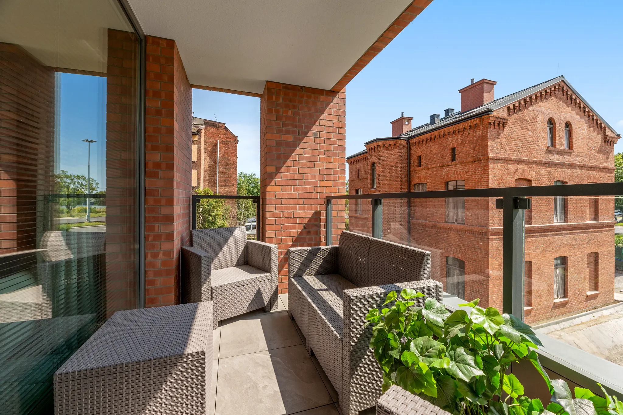 Balcony of a Scala apartment — woven armchairs, a table, glass balustrade and a view of a brick building