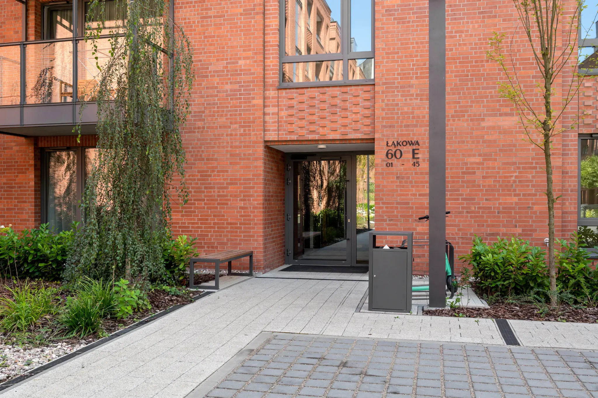 Entrance to the Scala building on Łąkowa — glazed doors in a brick façade, with a walkway and planting