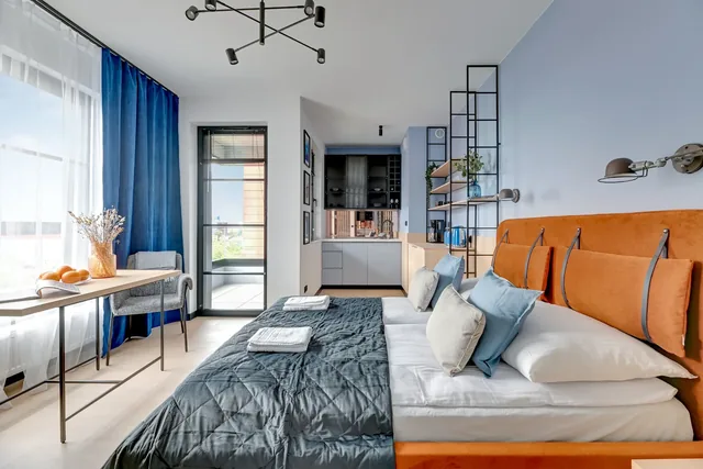 Gotowy apartament DOKI Living — sypialnia z niebieskimi zasłonami i pomarańczowym zagłówkiem