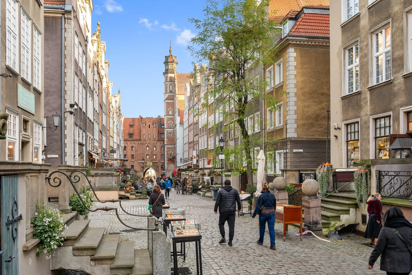 A cobbled street between historic townhouses, with pedestrians, doorsteps and a brick gateway in the distance.
