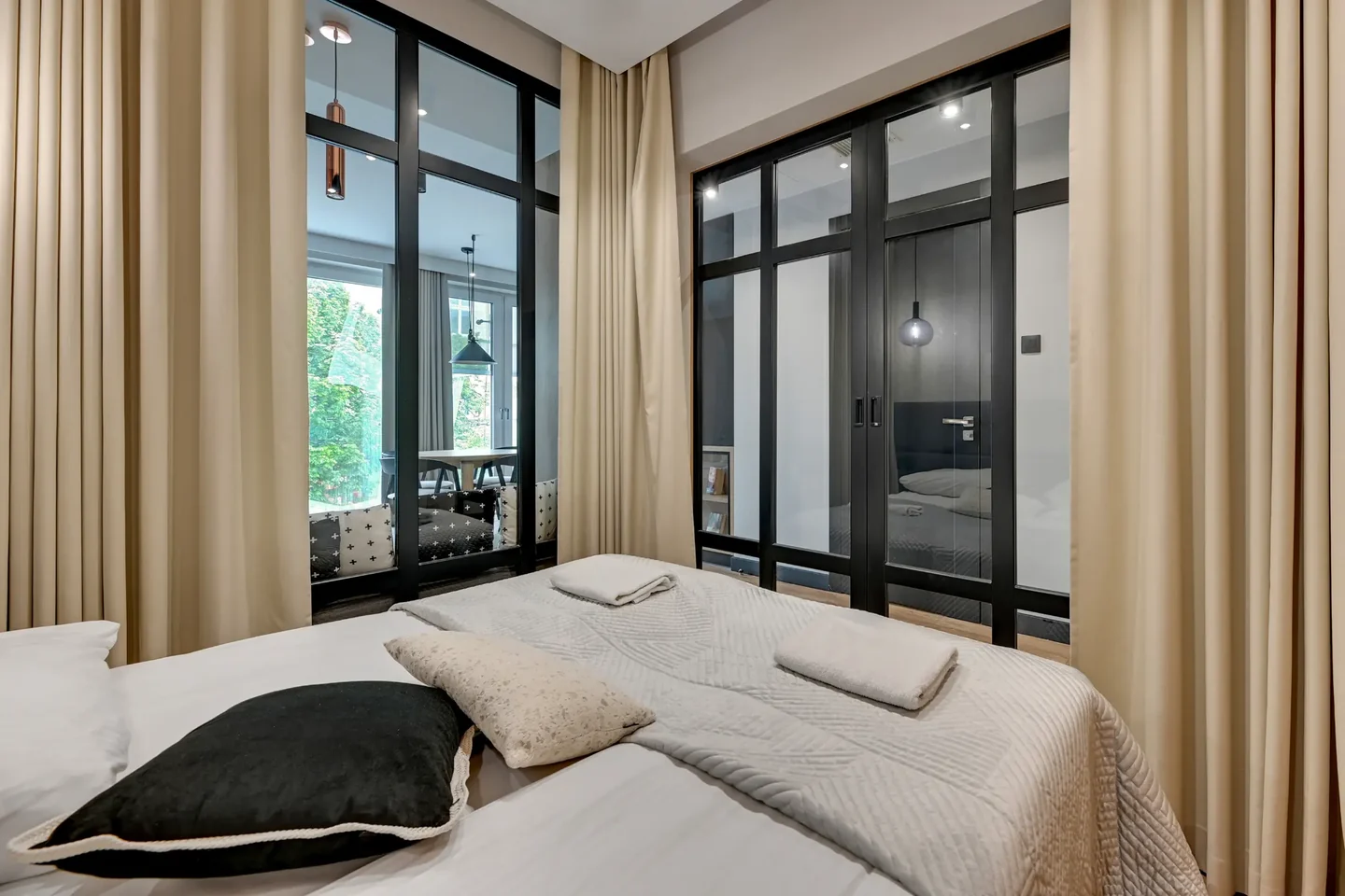 A bed with a light bedspread and folded towels beside glazed walls in black frames.