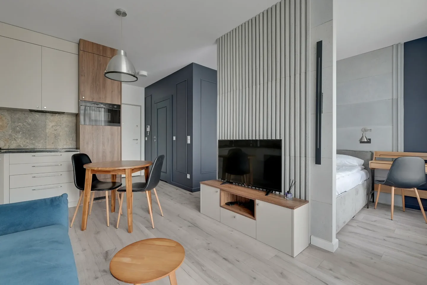 Interior with a kitchenette, round table, television and a visible sleeping area beside it.