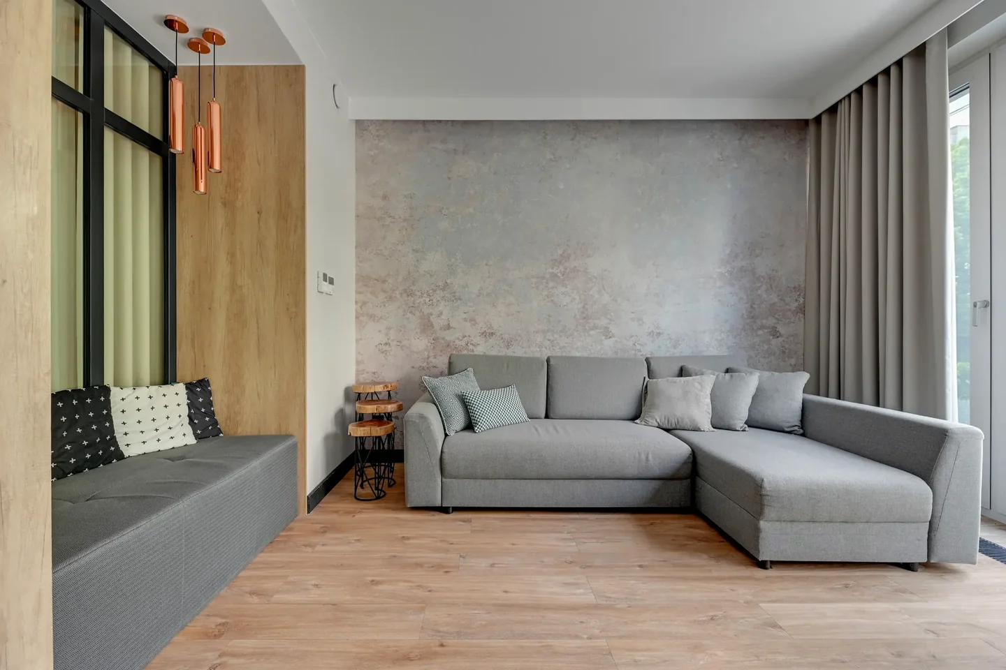 Living room with a grey corner sofa, an upholstered seat in an alcove and a large window with curtains.