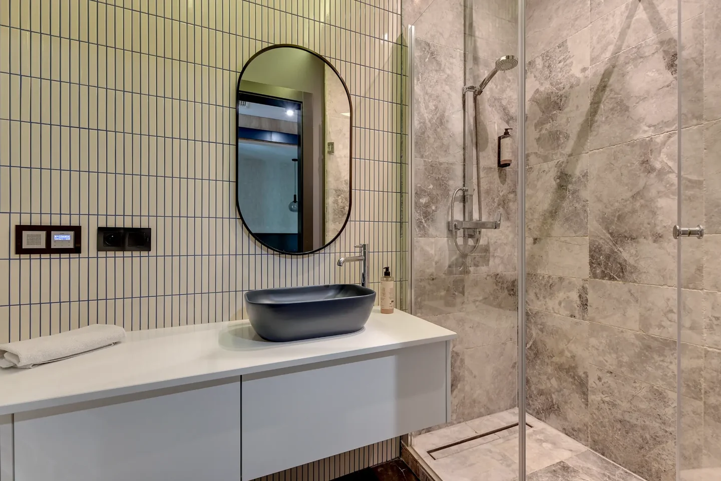 Bathroom with a dark countertop basin, an oval mirror and a glazed shower.